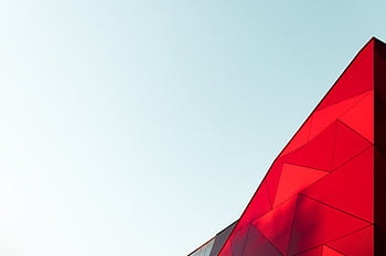 A vibrant red geometric facade of a modern building against a clear sky. HD wallpaper