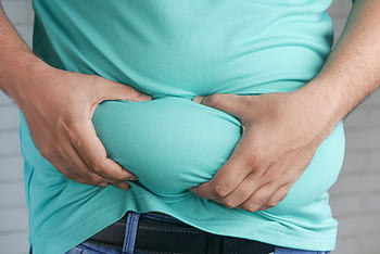 Close-up of hands gripping an overweight belly, depicting body fat focus. HD wallpaper