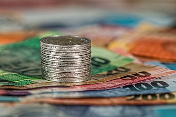 A stack of coins on top of various colored banknotes, symbolizing finance and currency. HD wallpaper