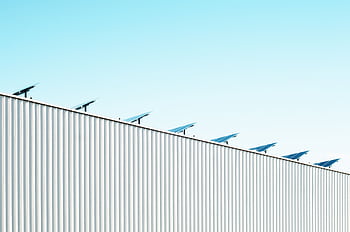 Corrugated steel building with solar panels under a clear blue sky, emphasizing sustainability. HD wallpaper