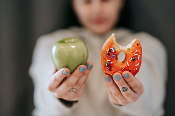 A close-up of a person holding an apple and a donut, symbolizing the choice between healthy eating and indulgence. HD wallpaper