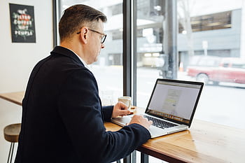 Adult male in cafe working on laptop, drinking coffee. Bright workspace with street view. HD wallpaper