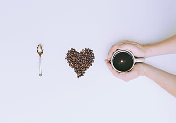 Coffee beans arranged in a heart shape with a mug and spoon on a white background. HD wallpaper