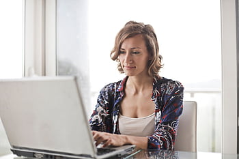 A woman typing on a laptop in a bright, modern home office setting. HD wallpaper