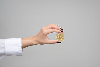 Close-up of a woman's hand holding a bitcoin coin against a neutral background. HD wallpaper