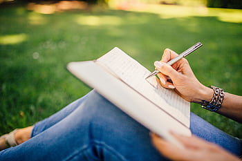 Person writes in a notebook on a sunny day. Focus on hands and pen outdoors. HD wallpaper