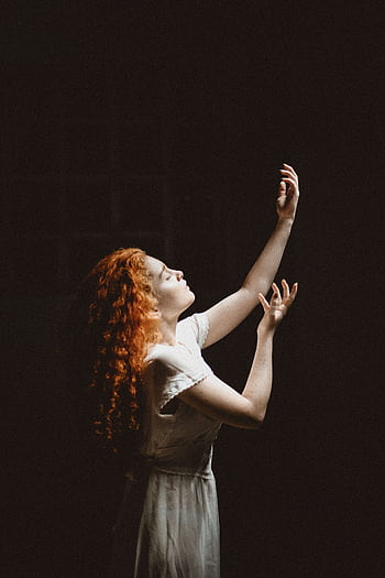 Elegant woman with red hair posing gracefully against a dark background, illuminated by soft light. HD phone wallpaper