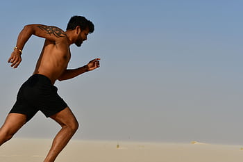 A muscular man sprinting shirtless through a desert, showcasing strength and determination. HD wallpaper
