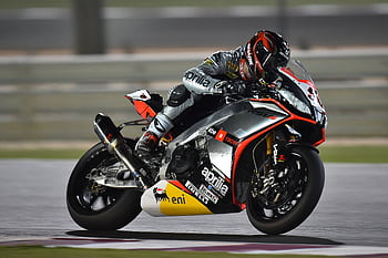 A professional motorbike racer leans into a turn during a high-speed race, showcasing agility and precision. HD wallpaper