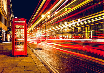 Red London booth at night with vibrant city light trails creating a dynamic urban scene. HD wallpaper