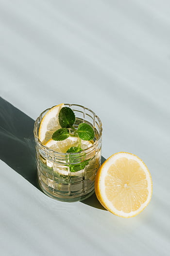 Icy lemon mint drink in glass, half lemon beside, casting cool shadows on table. HD phone wallpaper