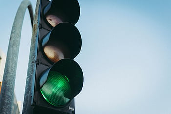 Close-up of a green traffic light against a clear blue sky, symbolizing go and safety. HD wallpaper