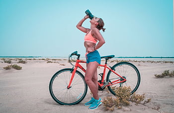 Athletic woman drinking water while biking in the Dubai desert landscape. HD wallpaper