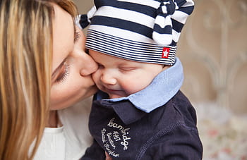 A mother lovingly kisses her smiling baby boy, creating a warm, affectionate scene. HD wallpaper
