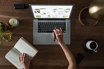 An overhead shot of a desk setup featuring a laptop, notebook, pen, and coffee cup, ideal for work and productivity themes. HD wallpaper