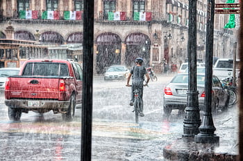 A cyclist rides through heavy rain in Morelia's urban street scene, Mexico. HD wallpaper