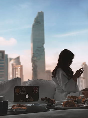 A serene morning scene of a woman relaxing with breakfast in a luxurious Bangkok hotel room. HD phone wallpaper