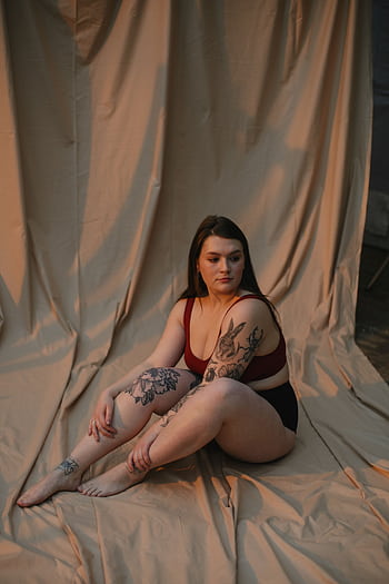 A tattooed woman posing thoughtfully against a curtain backdrop. HD phone wallpaper