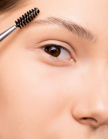 Detailed shot of a woman applying makeup to eyebrows using a brush, showcasing skincare routine. HD phone wallpaper