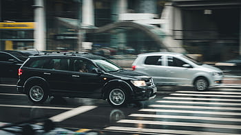 Vehicles speeding through a city street with a visible zebra crossing and blurred motion effect. HD wallpaper