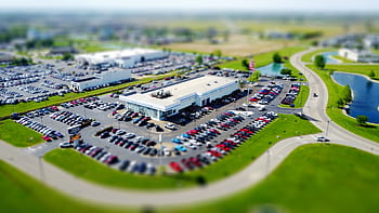 Aerial high-angle view of a bustling car dealership surrounded by parked cars in a green landscape. HD wallpaper
