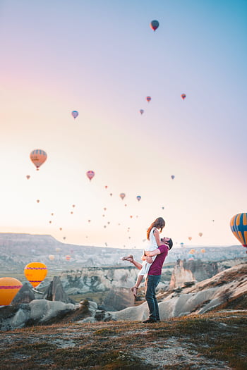 A couple shares a romantic moment at sunrise with hot air balloons in Cappadocia, Turkey. HD phone wallpaper