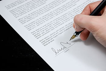 Close-up of a hand signing a formal document with a fountain pen, indicating agreement. HD wallpaper