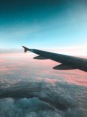 Dramatic view of an airplane wing over a colorful sunset cloudscape, capturing the essence of air travel. HD phone wallpaper