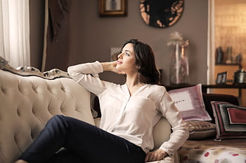 A serene woman enjoys a moment of reflection on a luxurious vintage sofa in a well-designed interior. HD wallpaper