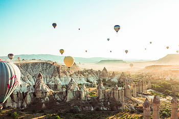 A stunning aerial view of hot air balloons floating over Cappadocia's rocky terrain during a sunny day. HD wallpaper