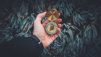 A close-up shot of a hand holding a vintage compass against a natural background. HD wallpaper