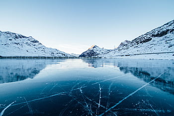 A serene winter landscape featuring a frozen lake surrounded by snow-covered mountains in Switzerland. HD wallpaper