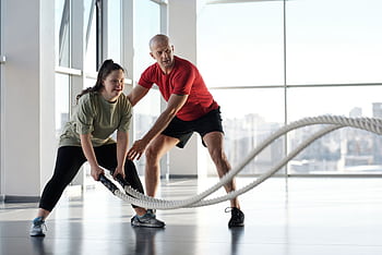 Woman and trainer engaging in rope workout in a bright gym, showcasing inclusivity and fitness motivation. HD wallpaper
