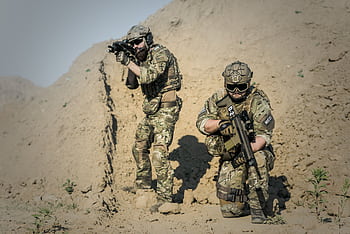 Two soldiers in camouflage gear equipped with weapons in a desert environment. HD wallpaper