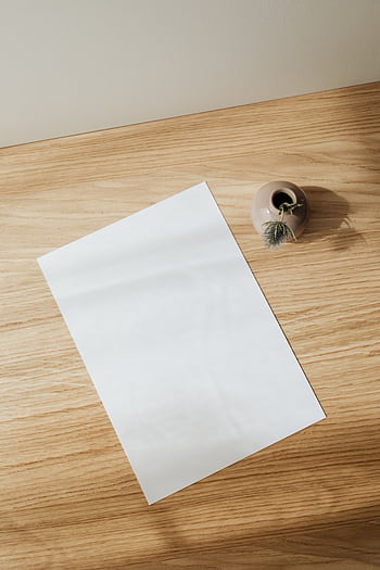 A minimalist setup featuring a blank sheet of paper and a ceramic vase on a wooden desk. HD phone wallpaper