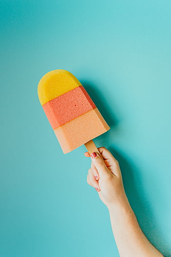 Vibrant multicolored popsicle against a blue backdrop, symbolizing summer refreshment. HD phone wallpaper