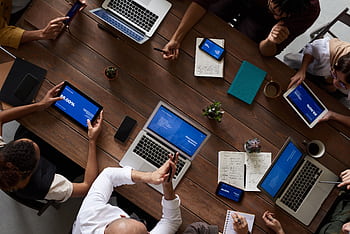 Overhead view of a diverse team discussing around a wooden table, using technology. HD wallpaper