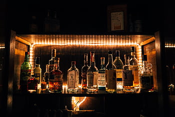 A stylish arrangement of various liquor bottles beautifully illuminated on a shelf in a dimly lit bar setting. HD wallpaper