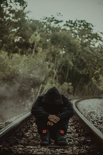 A person in a hoodie sits on empty train tracks, surrounded by nature. HD phone wallpaper
