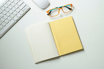 Top-down view of a clean workspace featuring a keyboard, mouse, stylish glasses, and an open notebook. HD wallpaper
