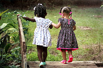Two young girls in colorful dresses walking hand in hand outdoors, embodying friendship and innocence. HD wallpaper