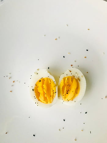 A close-up of a sliced boiled egg with pepper seasoning on a white plate, ideal for healthy meals. HD phone wallpaper