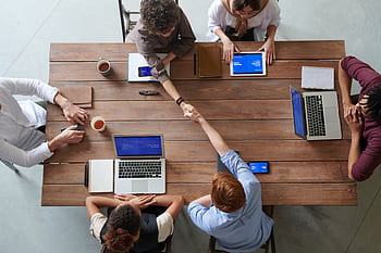 Overhead view of colleagues in a work meeting using laptops and tablets, emphasizing teamwork and technology. HD wallpaper