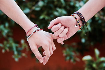 Two hands with colorful bracelets interlocked, symbolizing friendship and connection. HD wallpaper