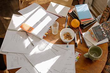 A cluttered study table with books, notes, and study materials in natural light for focused exam preparation. HD wallpaper