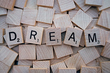 Close-up of wooden Scrabble tiles spelling the word 'DREAM', symbolizing creativity and imagination. HD wallpaper