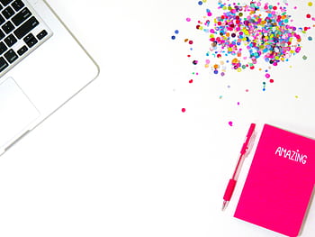 Bright flat lay with a laptop, pink notebook labeled 'AMAZING', pen, and colorful confetti. HD wallpaper