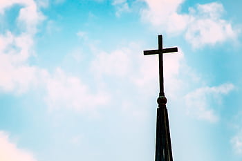 A church spire with a cross silhouetted against a bright blue sky with clouds. HD wallpaper