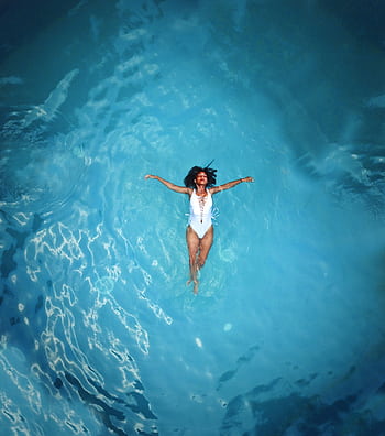 An African American woman in a swimsuit floats peacefully in a clear blue swimming pool. HD phone wallpaper
