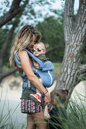 A loving mother embraces her children in a serene outdoor environment, highlighting family bonding. HD phone wallpaper